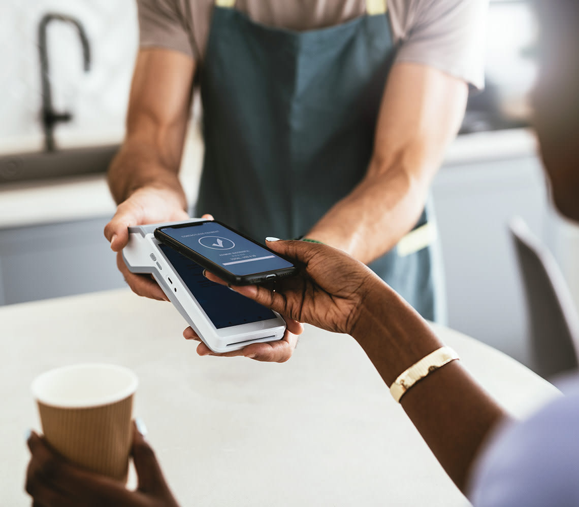 A woman makes payment with her mobile phone using the Transbank mobile POS while holding coffee in her other hand.